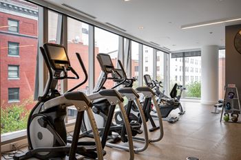 a row of exercise equipment in a gym with large windows
